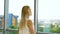 Zoom out of cheerful blonde woman looking out the window at cityscape