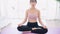 Zoom out of a sporty Asian woman practicing yoga on yoga mat, doing Ardha Padmasana exercise, meditating in Half Lotus pose,