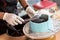 Zoom of pastry chef hand using rubber gloves smooth over melted chocolate on round blue cake