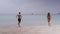 A zoom in shot of a joyful tourist couple running on the beach and dive into sea in a summer day