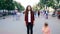 Zoom in time-lapse of beautiful girl with long curly hair standing in street looking at camera when many men and women