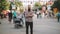 Zoom in timelapse of Young bearded man standing still at sidewalk in crowd traffic with people moving fast