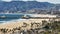 Zoomed aerial static shot of Pacific Park on the Santa Monica Pier and mountains in background. Sand beach on ocean
