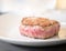 A zoomed-in picture with a blurry background of a medium-cooked beefsteak on a white plate placed on a table