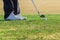 Zoomed in shot of a ball that is placed on a golf course and a golfer that is about to swing.
