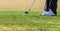Zoomed in shot of a ball that is placed on a golf course and a golfer that is about to swing.