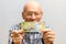 Ðžld bald man with glasses holds a banknote of 200 rubles in front of him.