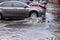 Ð’riving car on flooded road during flood caused by torrential rains. Cars float on water, flooding streets. Splash on car.