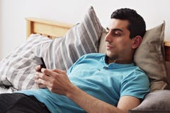 使用智能手机的年轻中东男性 在家说谎在床上库存图片 图片包括有
