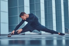 A Handsome Fitness Man In A Sportswear, Doing Stretching While Preparing For Serious Exercise In The Modern City Against Stock Images