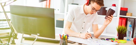 A Young Man With Glasses And Headphones Holds A Glass Of Coffee In His Hand And Draws A Marker On The Blackboard. Royalty Free Stock Photo A Young Man With Glasses And Headphones Holds A Glass Of Coffee In His Hand And Draws A Marker On The Blackboard. Royalty Free Stock Photo