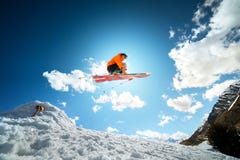 A Young Stylish Man In Sunglasses And A Cap Performs A Trick In Jumping With A Kicker Of Snow Against The Blue Sky And Royalty Free Stock Image