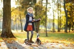 Aanbiddelijk jong meisje die haar autoped in een stadspark berijden op zonnige de herfstavond Preteen vrij kind die een rol berij stock afbeelding Aanbiddelijk jong meisje die haar autoped in een stadspark berijden op zonnige de herfstavond Preteen vrij kind die een rol berij stock afbeelding
