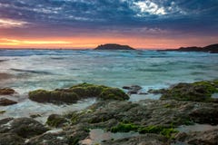 Aardzeegezicht met Groen Moss Covered Rocks, Vage Golven, Eiland en Kleurrijke Wolken bij Zonsopgang royalty-vrije stock fotografie Aardzeegezicht met Groen Moss Covered Rocks, Vage Golven, Eiland en Kleurrijke Wolken bij Zonsopgang royalty-vrije stock fotografie