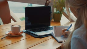 Abschluss oben der Geschäftsfrau schreibt einen Stift in ein Notizbuch, das Laptop betrachtet stock footage Abschluss oben der Geschäftsfrau schreibt einen Stift in ein Notizbuch, das Laptop betrachtet stock footage
