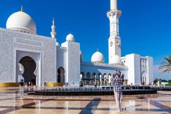 Abu Dhabi, Emiratos Árabes Unidos - 13 de dezembro de 2018: a menina olha a fachada da mesquita grande imagem de stock Abu Dhabi, Emiratos Árabes Unidos - 13 de dezembro de 2018: a menina olha a fachada da mesquita grande imagem de stock