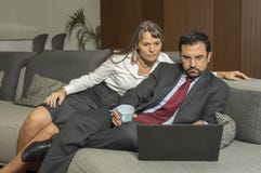 Acople em casa no formalware com funcionamento do homem e observação da mulher foto de stock Acople em casa no formalware com funcionamento do homem e observação da mulher foto de stock