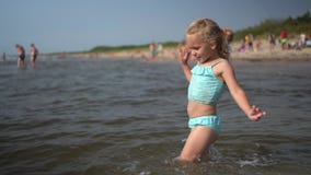 Active playful little girl dance wading through sea water waves. Funny child