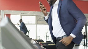 Addestramento maschio afroamericano serio sulla pedana mobile e parlare sul telefono cellulare video d archivio Addestramento maschio afroamericano serio sulla pedana mobile e parlare sul telefono cellulare video d archivio