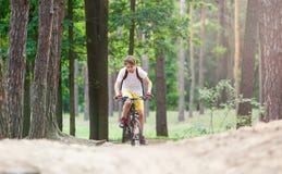 Adolescent d'enfant dans le T-shirt blanc et shorts jaunes sur le tour de bicyclette dans la forêt au ressort ou à l'été Recyclag photographie stock Adolescent d'enfant dans le T-shirt blanc et shorts jaunes sur le tour de bicyclette dans la forêt au ressort ou à l'été Recyclag photographie stock