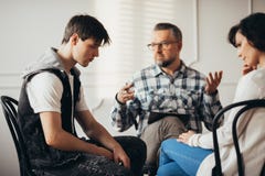 Adolescente triste che ascolta il suo psychatrist durante la visita in ospedale psichiatrico con sua madre fotografie stock Adolescente triste che ascolta il suo psychatrist durante la visita in ospedale psichiatrico con sua madre fotografie stock