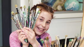 Cute happy girl smiling to the camera holding bunch of paintbrushes