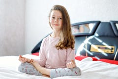 Adorable happy little kid girl after sleeping in his white bed in colorful nightwear. School child making baby yoga stock photo Adorable happy little kid girl after sleeping in his white bed in colorful nightwear. School child making baby yoga stock photo