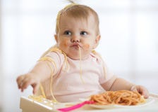 Adorable little baby one year eating pasta indoor. Funny toddler child with spaghetti. Cute kid and healthy food.