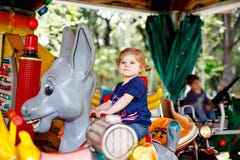 Adorable little toddler girl riding on animal on roundabout carousel in amusement park. Happy healthy baby child having stock photo Adorable little toddler girl riding on animal on roundabout carousel in amusement park. Happy healthy baby child having stock photo