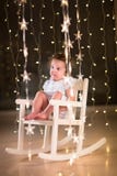 Adorable toddler girl in a white rocking chair in dark room with Christmas lights royalty free stock images Adorable toddler girl in a white rocking chair in dark room with Christmas lights royalty free stock images