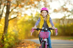 Adorable young girl riding a bike in a city park on sunny autumn day. Active family leisure with kids royalty free stock photo Adorable young girl riding a bike in a city park on sunny autumn day. Active family leisure with kids royalty free stock photo