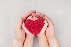 Adult and child holding red heart in hands top view. Family relationships, health care, pediatric cardiology concept.