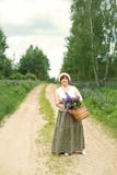Adult woman walks through the woods park with a wicker basket with a bouquet of lupine flowers stock photo Adult woman walks through the woods park with a wicker basket with a bouquet of lupine flowers stock photo