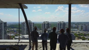 Aerial shot of builders team on construction site back rear view of workman discussing plan of project stock video footage Aerial shot of builders team on construction site back rear view of workman discussing plan of project stock video footage