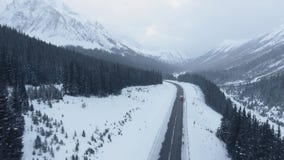 Aerial video from a height above the path crossing the mountain area in deep winter in Kananaskis, Alberta, Canada