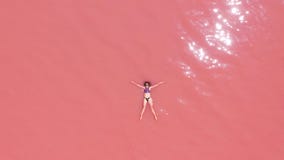 Aerial view. A beautiful young girl lies on in the pink lake, a bikini, sunglasses, pink clear water, a top view stock video footage Aerial view. A beautiful young girl lies on in the pink lake, a bikini, sunglasses, pink clear water, a top view stock video footage