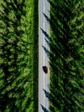 Aerial view of a country road with red car in the middle of green summer forest stock photo Aerial view of a country road with red car in the middle of green summer forest stock photo