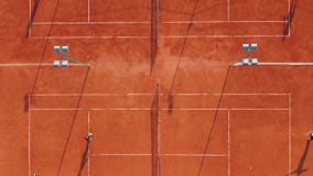 Aerial view. Players are playing tennis on orange court. stock footage Aerial view. Players are playing tennis on orange court. stock footage