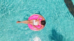 Aerial view of a young brunette woman swimming on an inflatable big donut with a laptop in a transparent turquoise pool. stock images Aerial view of a young brunette woman swimming on an inflatable big donut with a laptop in a transparent turquoise pool. stock images