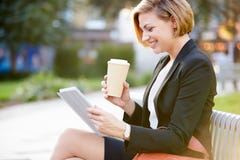 Affärskvinna On Park Bench med kaffe genom att använda den Digital minnestavlan arkivbilder Affärskvinna On Park Bench med kaffe genom att använda den Digital minnestavlan arkivbilder
