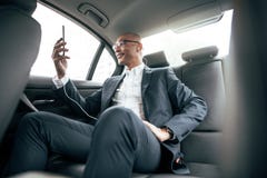 Affärsmansammanträde i bilen som ser hans mobiltelefon royaltyfri bild Affärsmansammanträde i bilen som ser hans mobiltelefon royaltyfri bild