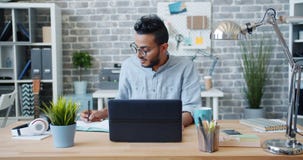 African American guy using laptop in office then writing in notebook stock video African American guy using laptop in office then writing in notebook stock video