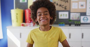 African american schoolboy standing, smiling in classroom looking at camera learning about recycling