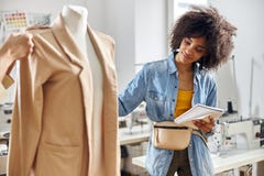 African-American Woman With Notebook Looks At Stylish Beige Jacket While Designer Measures Detail In Studio Royalty Free Stock Photography African-American Woman With Notebook Looks At Stylish Beige Jacket While Designer Measures Detail In Studio Royalty Free Stock Photography