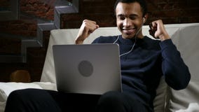 African Man Listening Music on Laptop and Dancing at Night