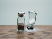 Agitatore di sale capovolto equilibrato su sale rovesciato accanto all'agitatore ribaltato del pepe fotografia stock Agitatore di sale capovolto equilibrato su sale rovesciato accanto all'agitatore ribaltato del pepe fotografia stock