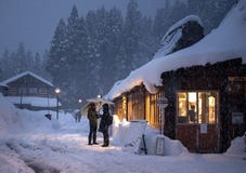 Ainokura, Japan - December 30, 2018: Paar die zich voor de enige winkel in dit kleine dorp bevinden, die beschermen tegen h stock foto's Ainokura, Japan - December 30, 2018: Paar die zich voor de enige winkel in dit kleine dorp bevinden, die beschermen tegen h stock foto's