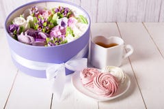 Airy and sweet handmade marshmallows on a white saucer next to a cup of tea and a box with a bouquet of marshmallow flowers