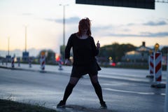 Aktive Reisendt?nzerfrau, die an einem Stra?enbaustandort zur Sonnenuntergangzeit mit den Autolichtern ?berschreiten durch das Tr lizenzfreies stockbild Aktive Reisendt?nzerfrau, die an einem Stra?enbaustandort zur Sonnenuntergangzeit mit den Autolichtern ?berschreiten durch das Tr lizenzfreies stockbild