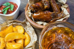 Ali di pollo con salsa fragrante e pungente con i semi di sesamo Un vetro di birra fredda fresca e delle patate fritte con il pom Fotografia Stock Ali di pollo con salsa fragrante e pungente con i semi di sesamo Un vetro di birra fredda fresca e delle patate fritte con il pom Fotografia Stock